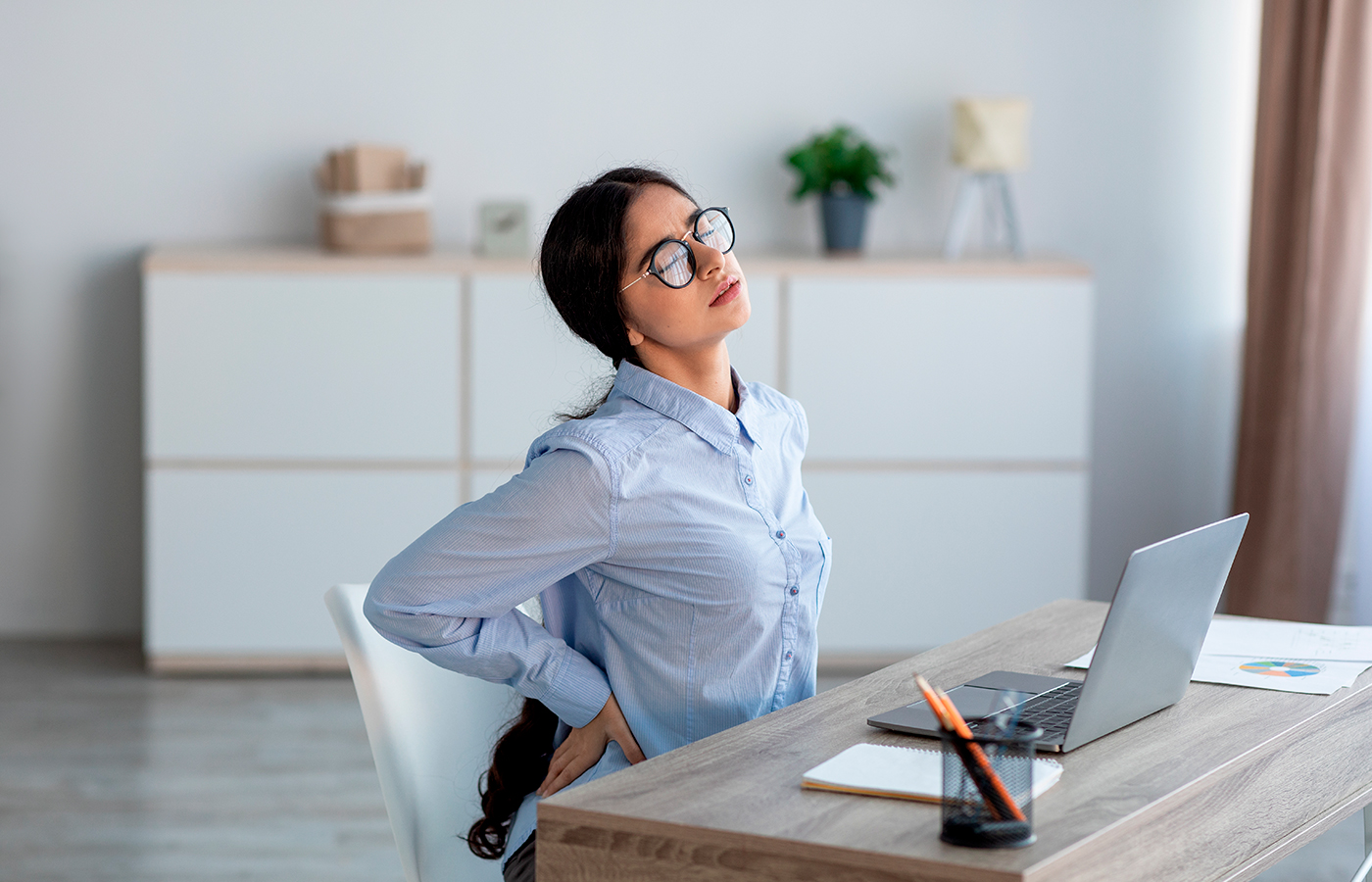 a woman experiencing back pain from poor posture while sitting at her desk